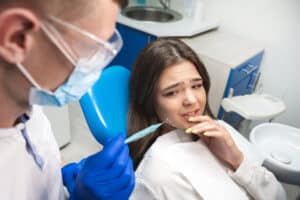 Anxious girl in dentist's chair looking at dental tools, who could benefit from dental sedation