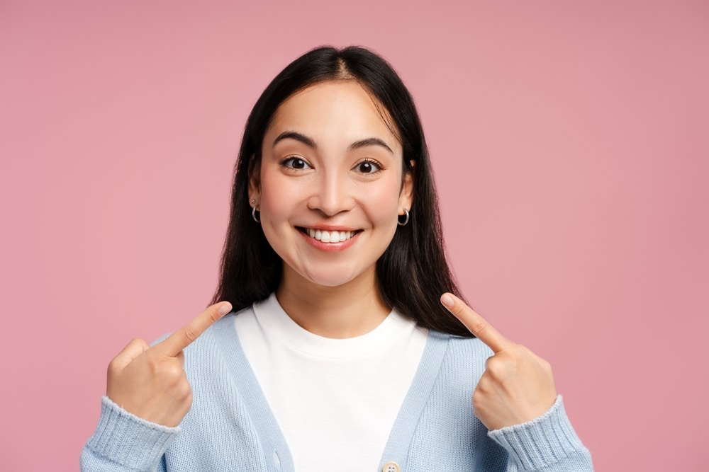 Woman smiling and pointing to healthy, beautiful teeth after getting CEREC crowns.